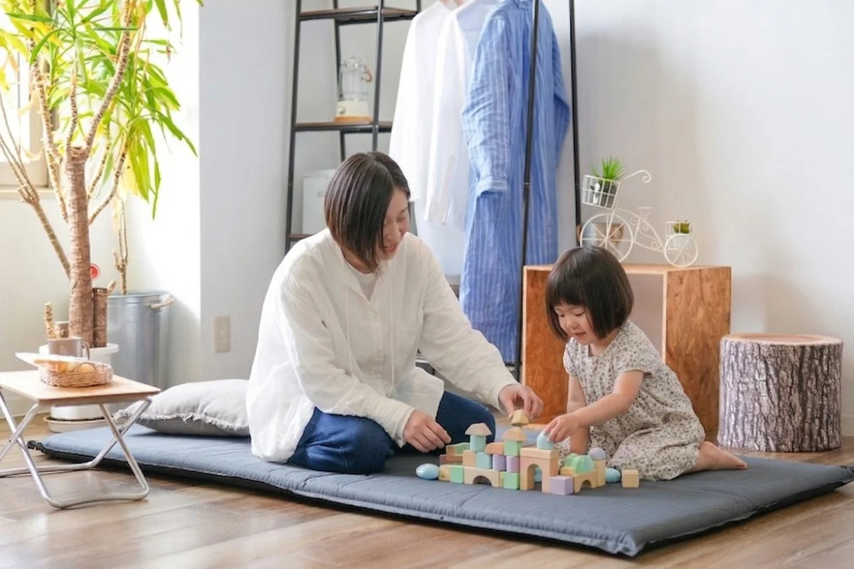 室内でフロアマットに座り、母親と子供が積み木で遊んでいる心温まる一場面