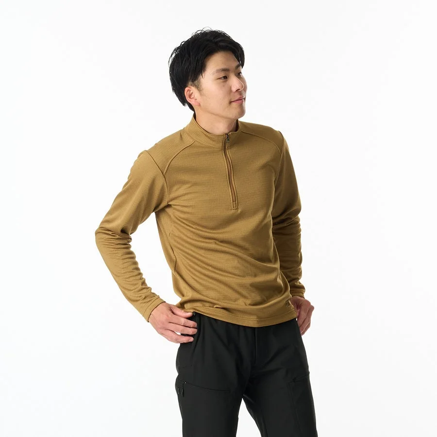 白い背景の前で、茶色のハーフジップ長袖シャツと黒いパンツを着用した男性が、右を向いて立っている全身ショット