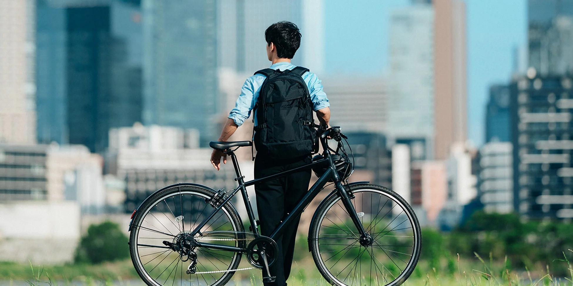 都市のビル群を背景に立つ男性と自転車
