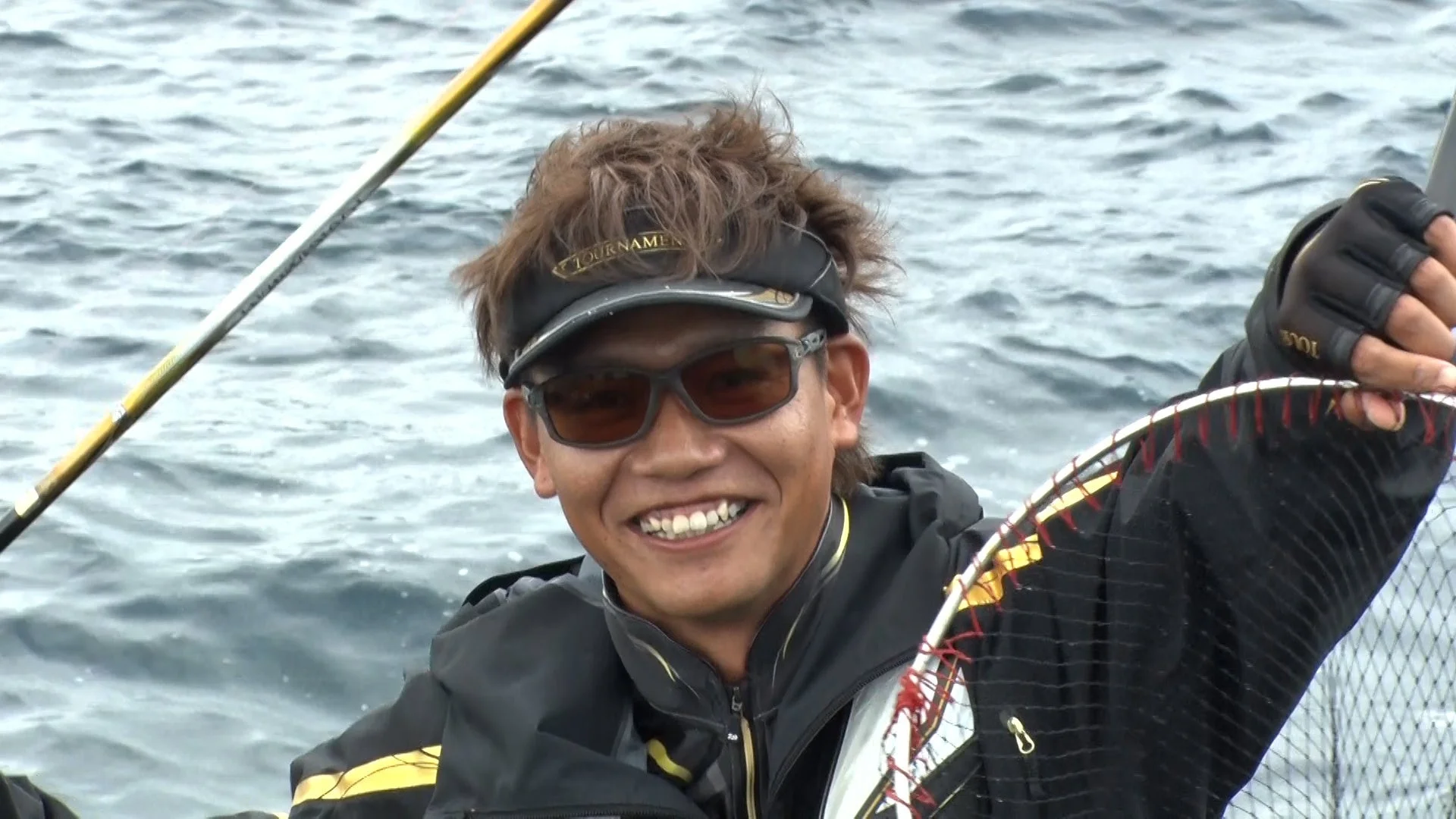 笑顔でタモ網と釣り竿を持つ池田翔悟氏