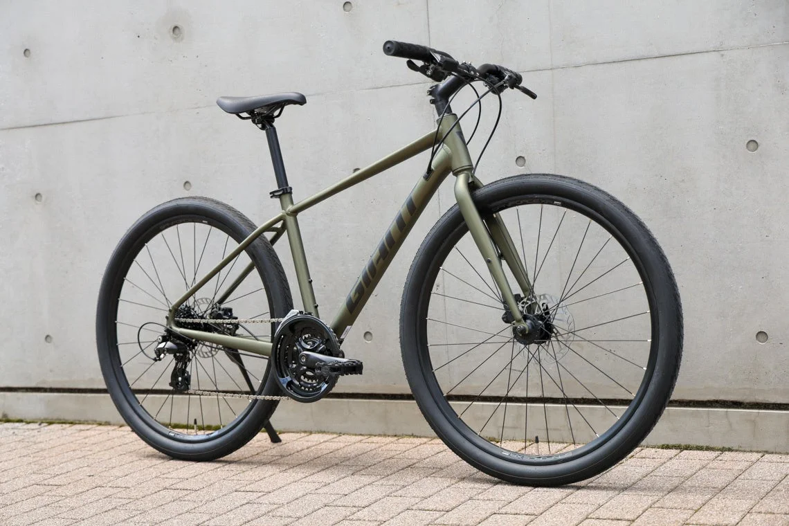 カーキ色のGIANT製クロスバイクが、コンクリートの壁を背景に停められています