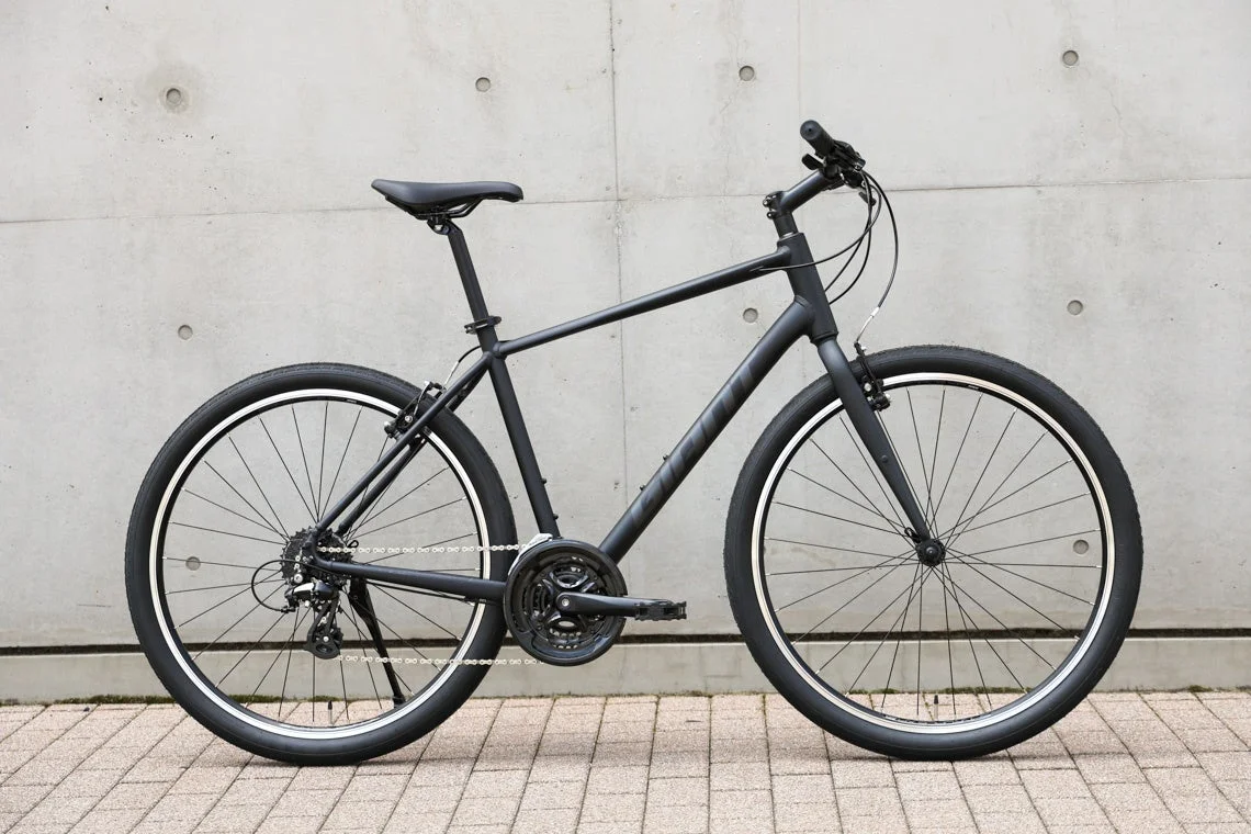 マットブラックのクロスバイクがコンクリートの壁を背景に置かれています