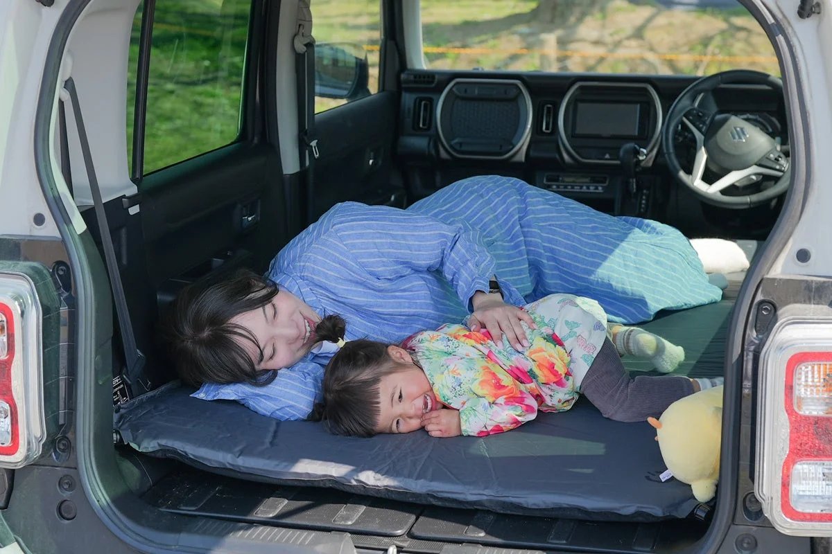 軽自動車の荷室で、母親と子供が笑顔で寄り添いながらくつろいでいる様子