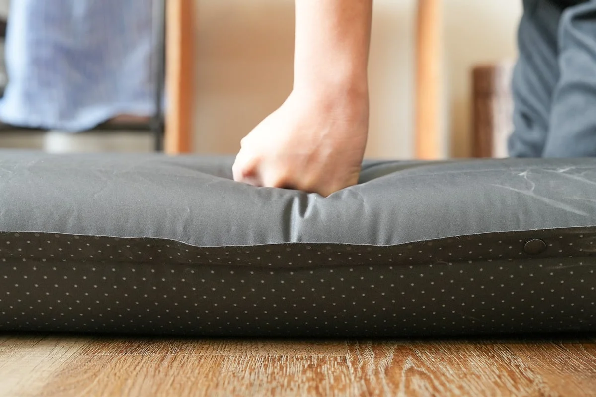 手がダークグレーのクッションまたはマットレスを押し込んでおり、その柔らかさや弾力性を示しています